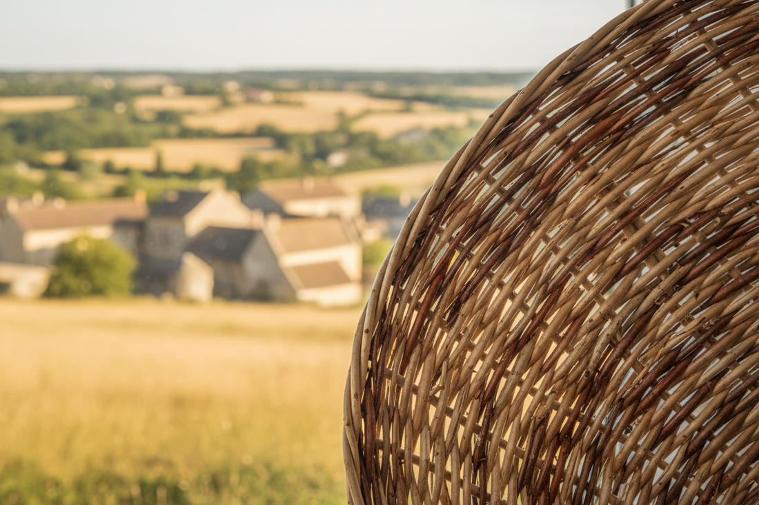 un panier en osier avec en fond un vilage et un champ 